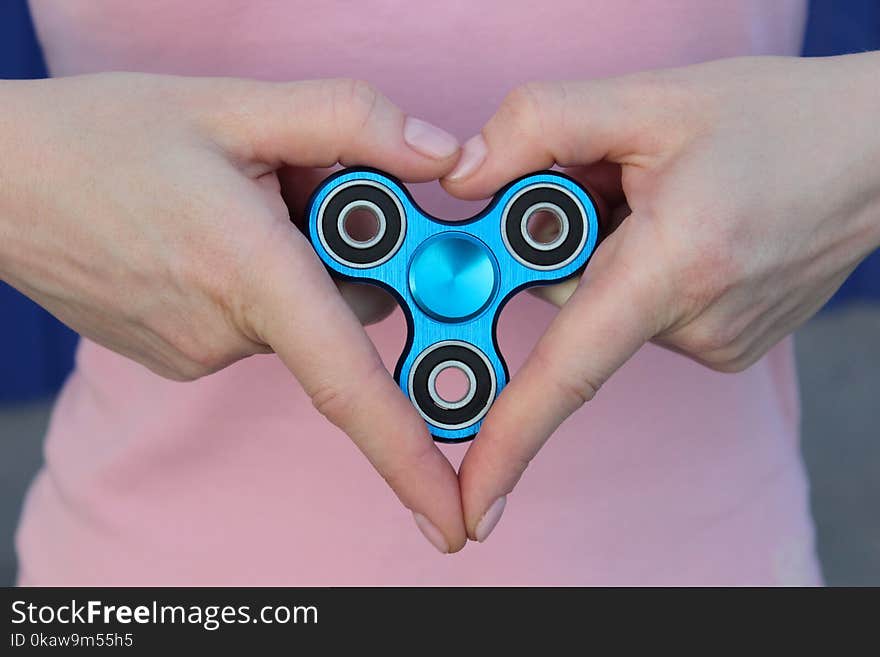 girl is playing blue metal spinner in hands on the street, woman playing with a popular fidget spinner toy, girl love anxiety relief toy, anti stress and relaxation fidgets, sign of love.