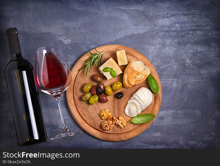 Bottle and glass of wine with cheese, olives, bread, nuts and basil on dark background. Wine and food concept. View from above, top