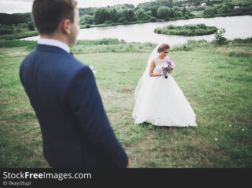 Newly married couple running and jumping in park while holding hands.