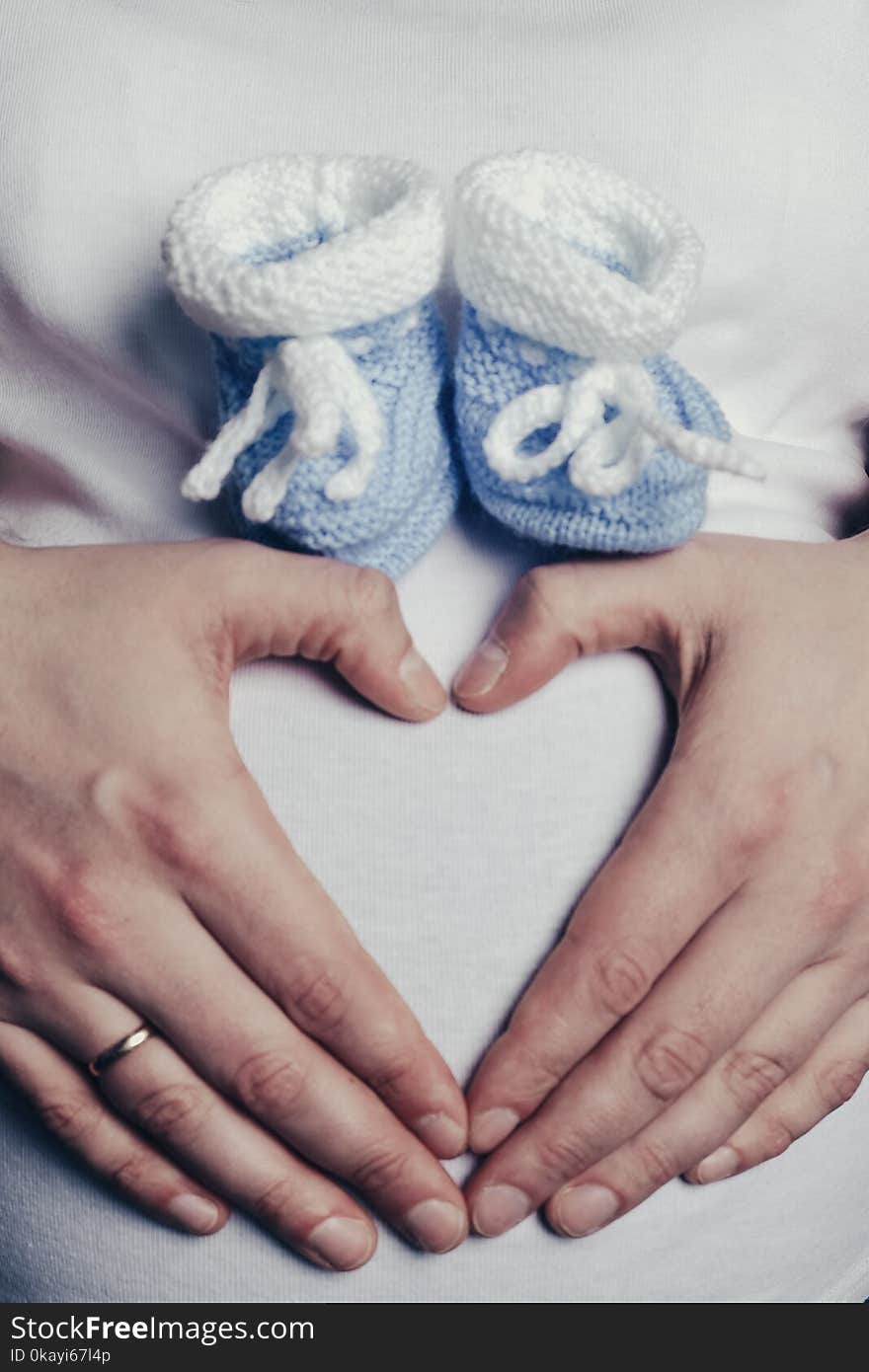 Mom`s hands in the shape of heart with booties on the stomach close-up, upright