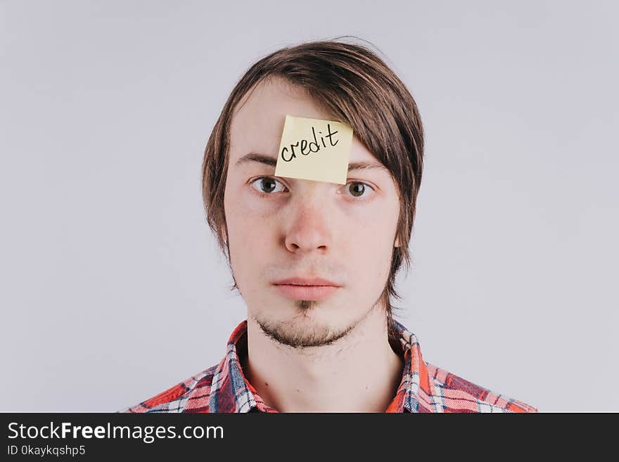 Sad man looks directly, the sticker is glued on the forehead with the word credit . A young guy is upset by debt, credit