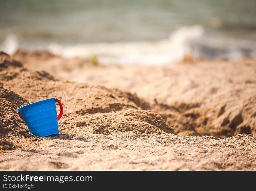 A plastic pail in the sand. Baby bucket seashore. Working tool against the background of the sea coast. Children`s plastic bucket.