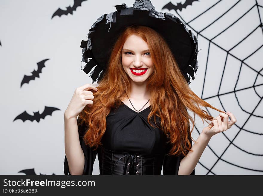 Halloween witch concept - Happy Halloween Witch holding posing over dark grey studio background with bat and spider web.