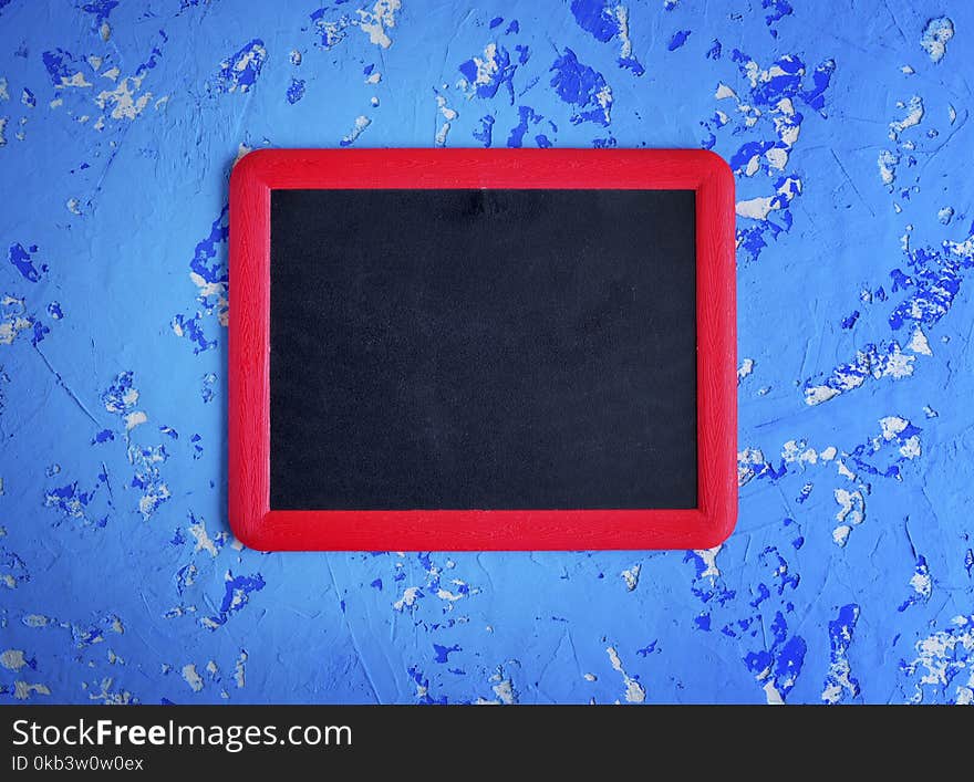 Empty black chalk board in a red frame on a worn blue surface, close up