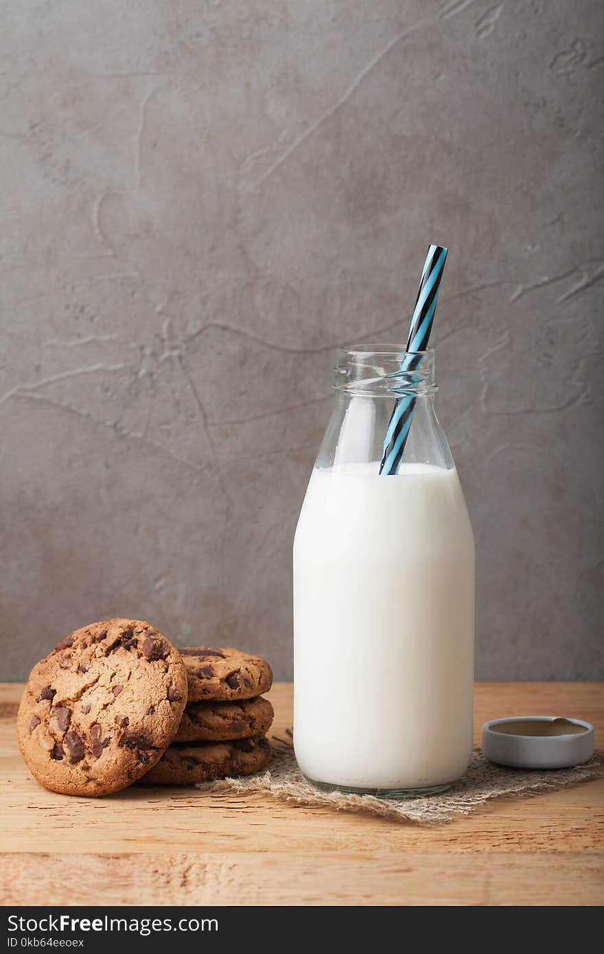 Bottle with milk and chocolate chip cookies on dark background with copy space.