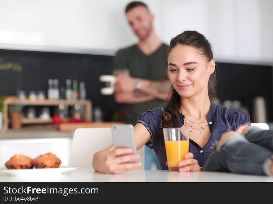 Happy Couple Using Smartphone Sitting In Kitchen