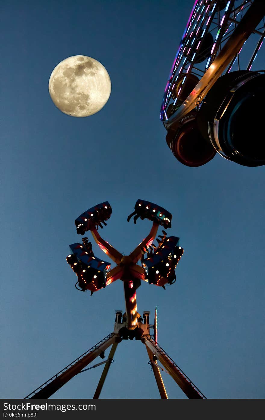 Fair rides at a fair at night with the moon. Fair rides at a fair at night with the moon