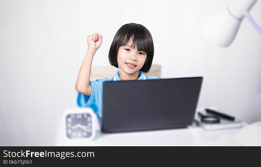 Cute child thinking and typing laptop. Asian child girl working on work desk. She sitting on chair on white gray fabric background.