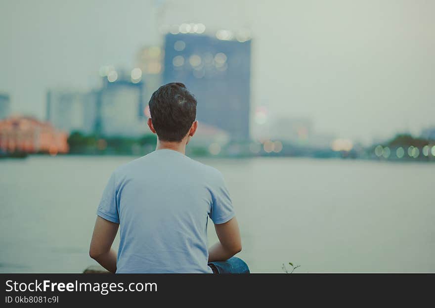 Photo of Man Wearing Blue Shirt Sitting Looking on High-rise Buildings