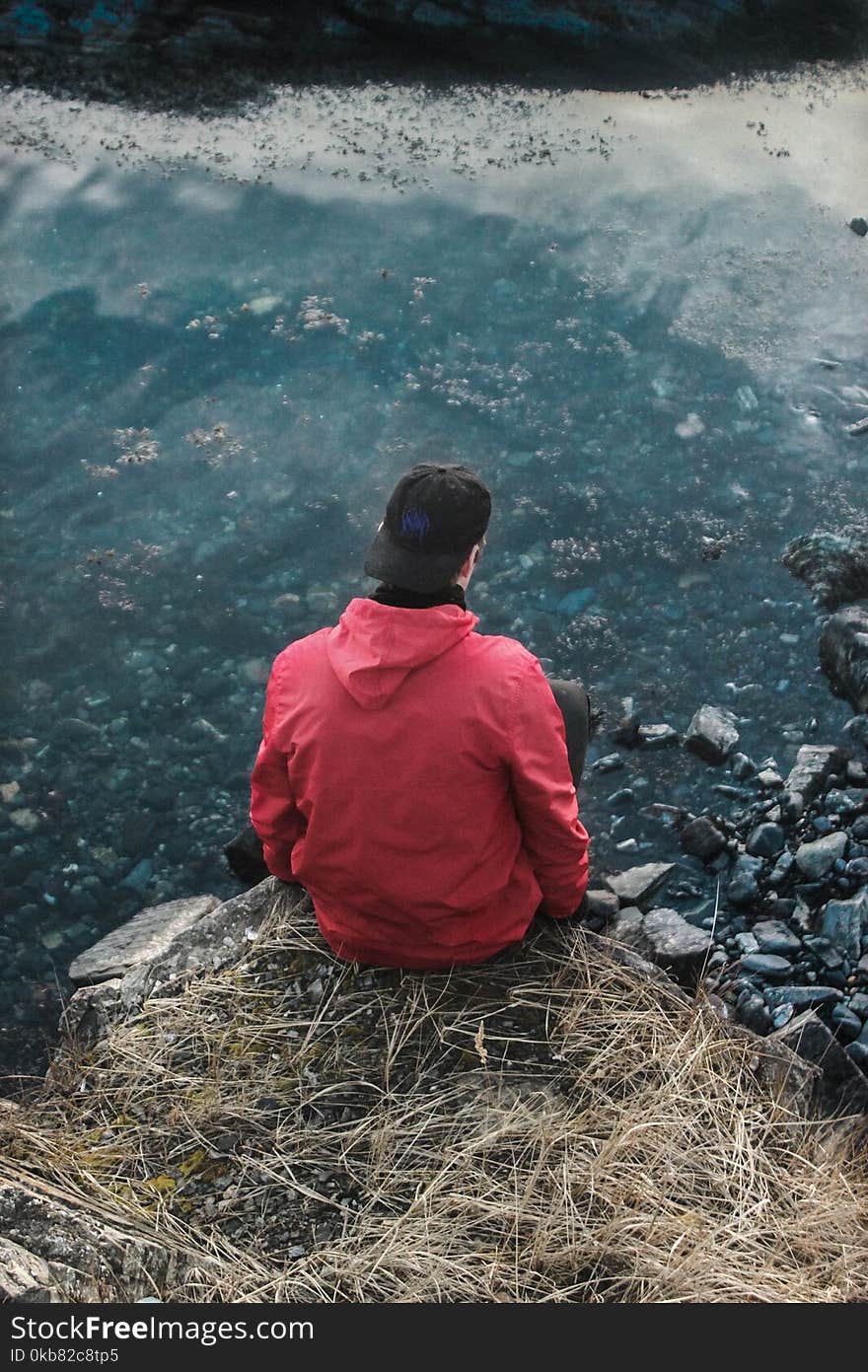 Man in Red Hoodie Sitting on Cliff