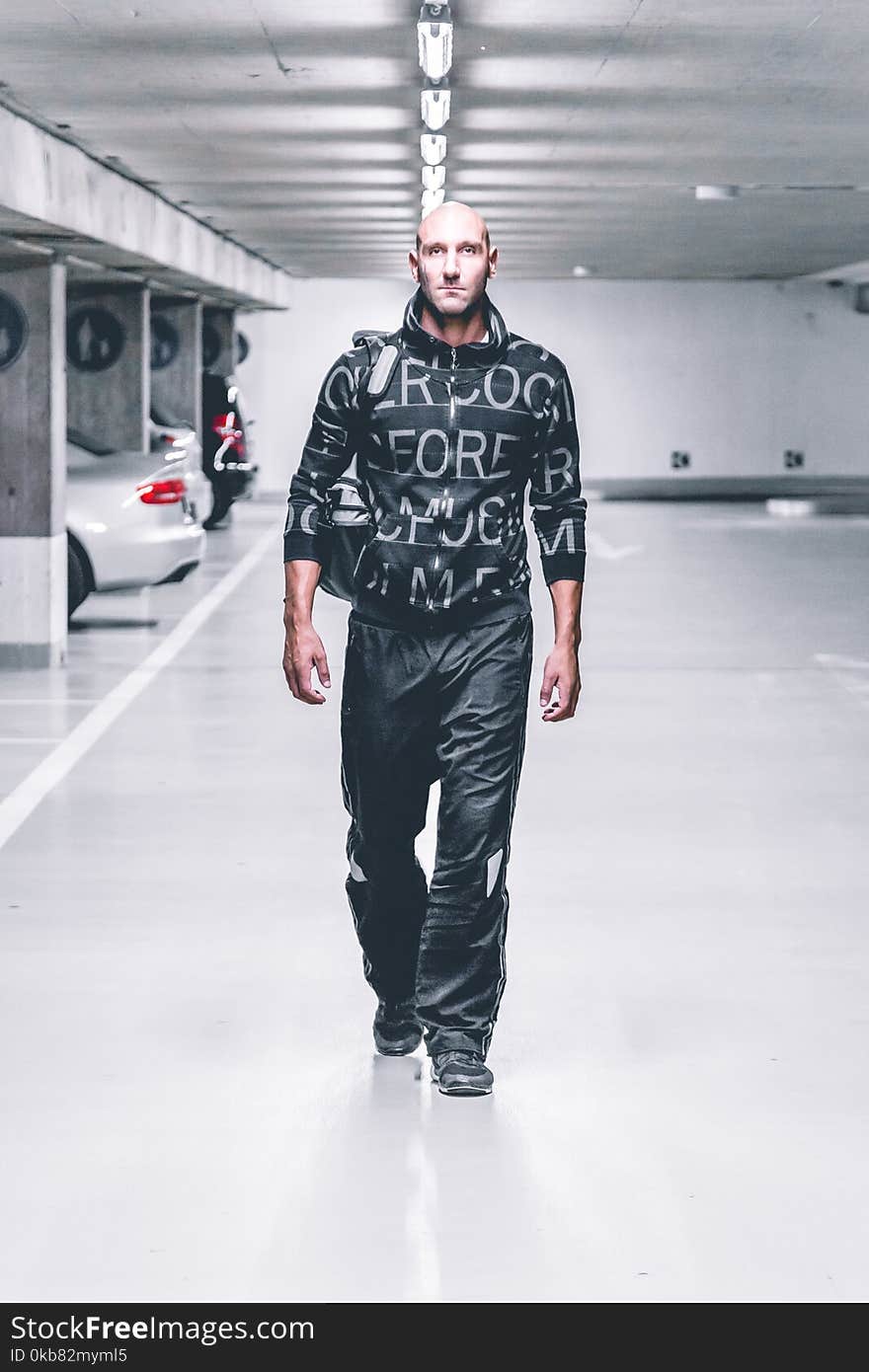 Photo of Man in Black Pants and Top Walking in Parking Lot