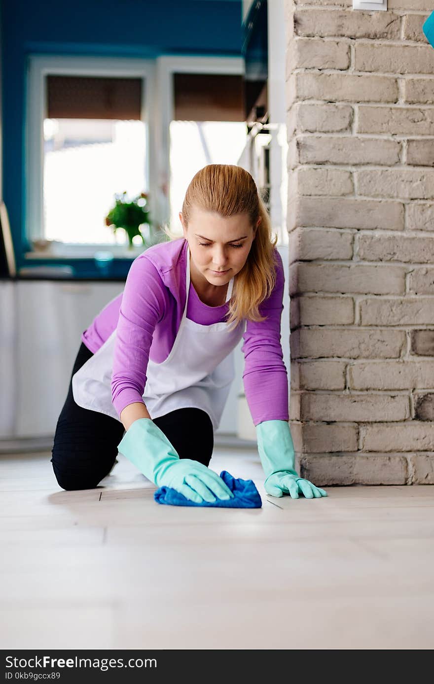 Young woman in white apron washing floor on her knees.