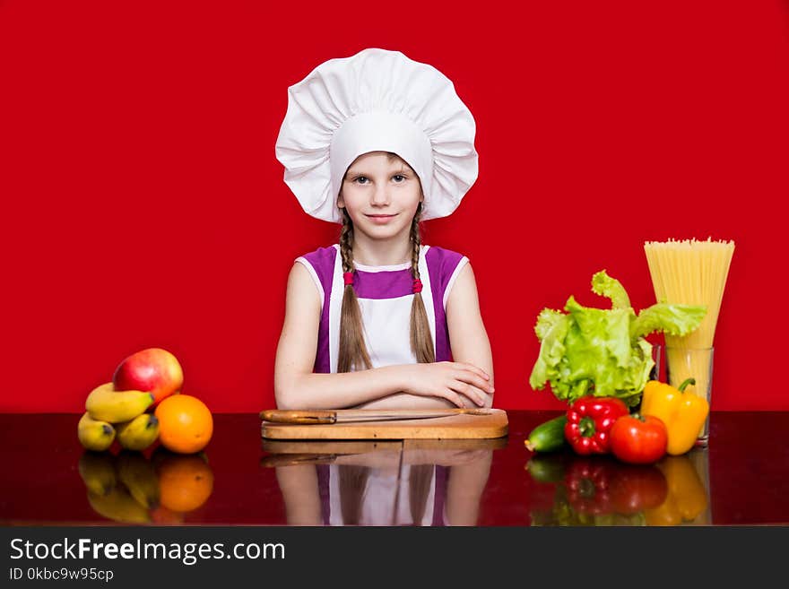 Happy little girl in chef uniform cuts fruit in kitchen. Kid chef. Cooking Process Concept