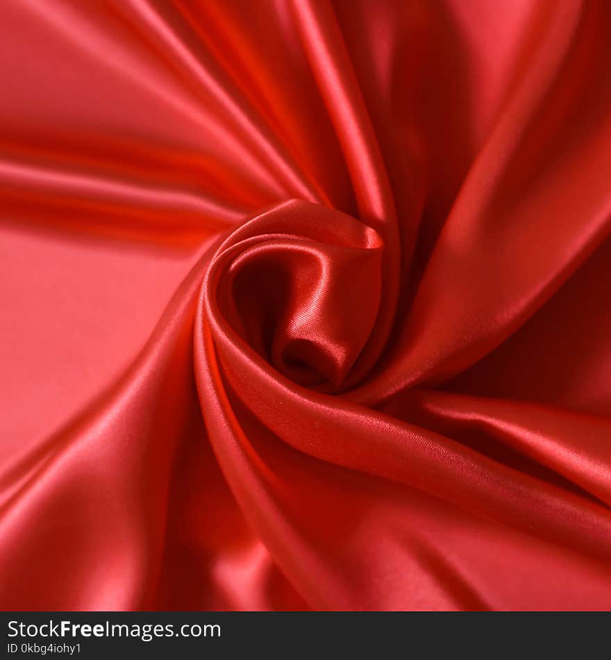 Close up of ripples in shape of rose flower on red silk fabric. Satin textile background.