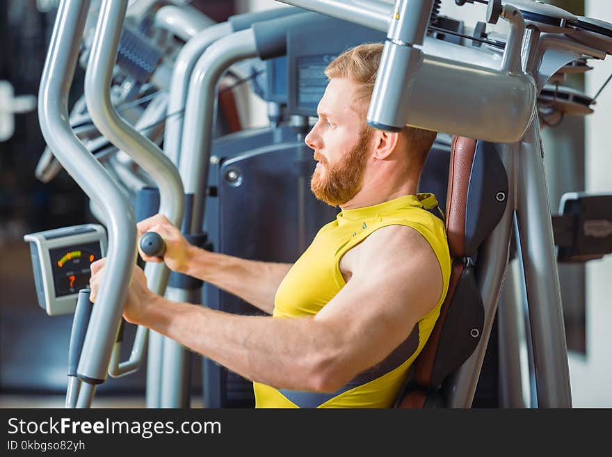 Portrait of a handsome bodybuilder smiling and looking at camera while exercising at a modern fitness machine for pectoral fly and deltoid workout