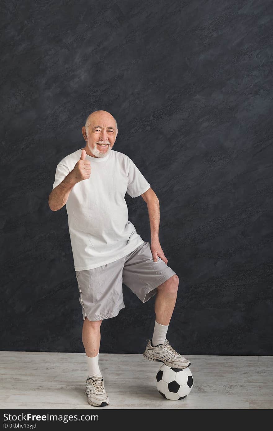 Smiling senior man posing with soccer ball showing thumb up gesture, black background. Hobby, active lifestyle in any age and motivation, copy space. Smiling senior man posing with soccer ball showing thumb up gesture, black background. Hobby, active lifestyle in any age and motivation, copy space