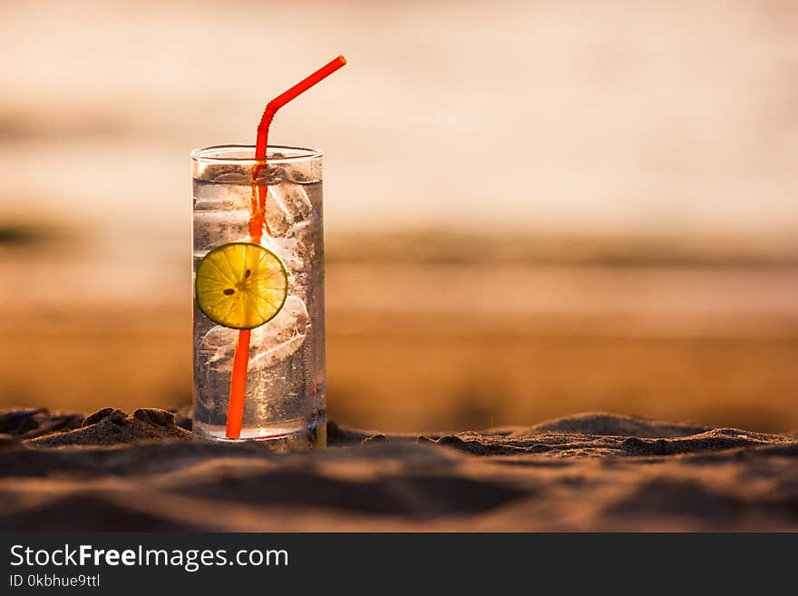 Picture of a glass of Gin Tonic with straw and lime slice on the beach, at sunset. Long Beach, Ko Lanta, Thailand.