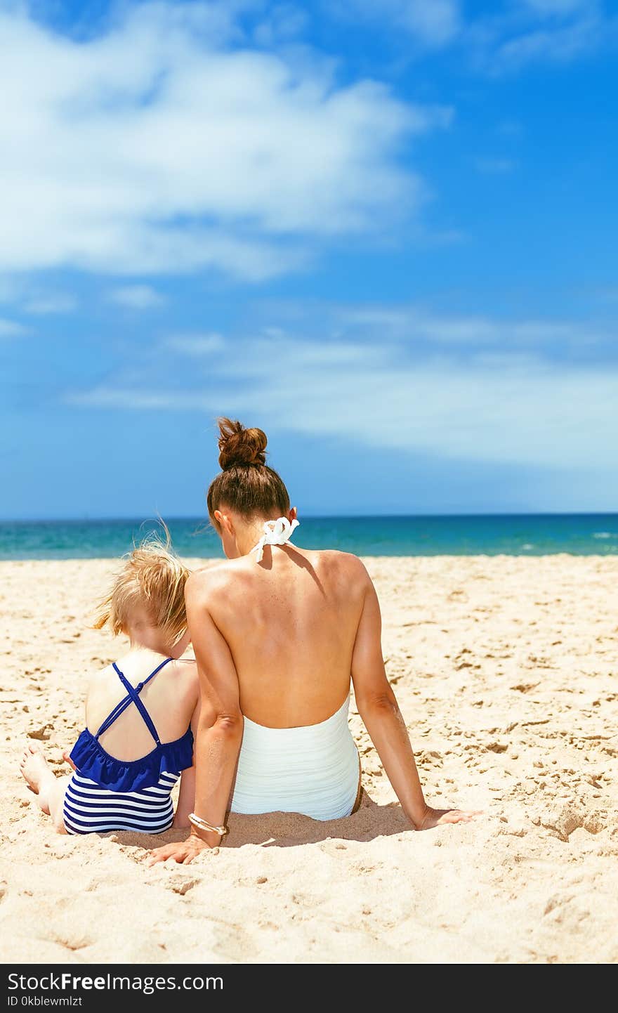 Seen from behind young mother and child in swimwear on beach