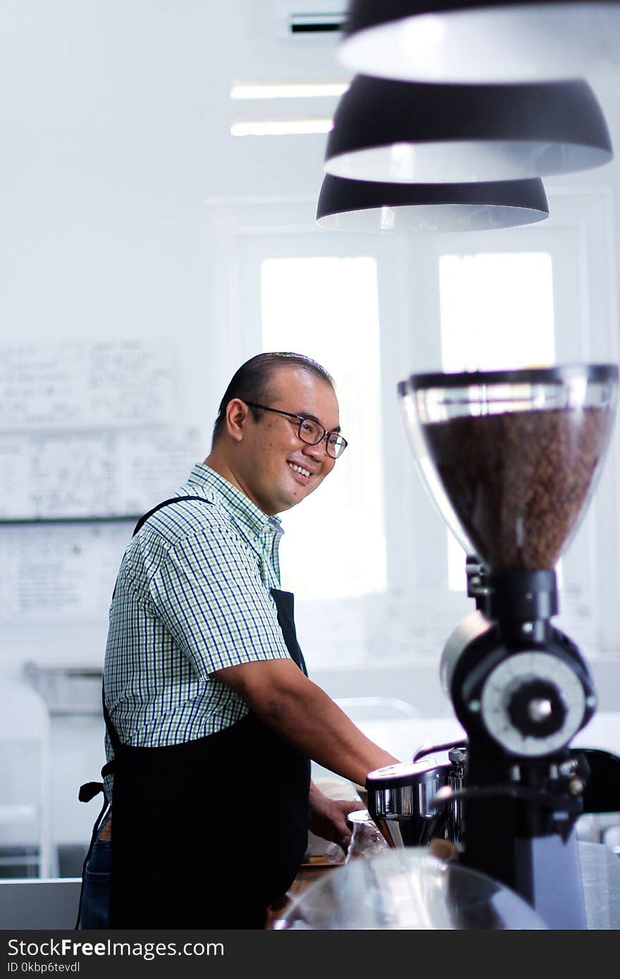 Man Wearing Plaid T-shirt And Black Apron in Front of Coffeemaker