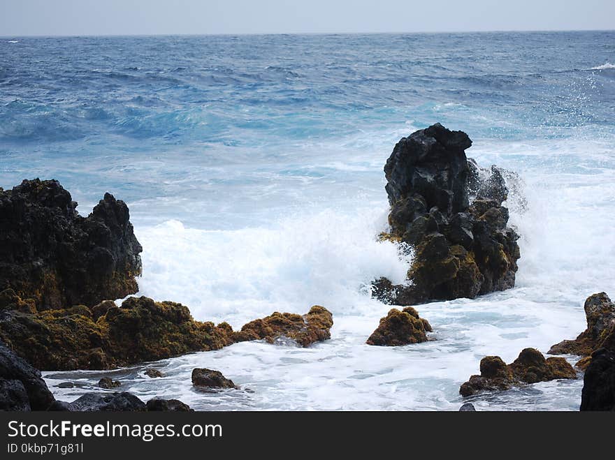 Big Rocks Surrounded by Body of Water Under Blue Sky at Daytime