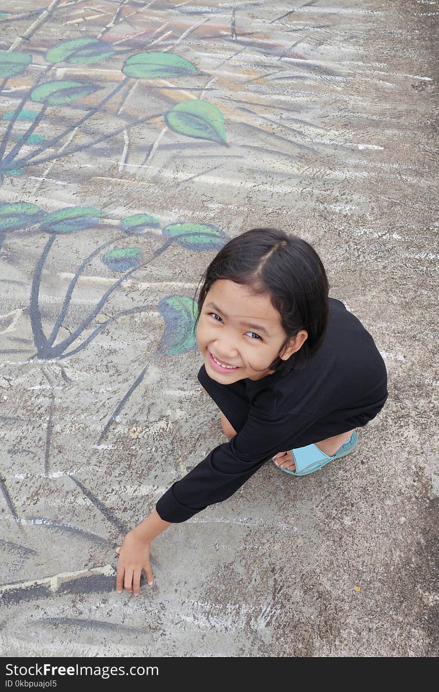 A little girl with a smile sitting on a painted cement background