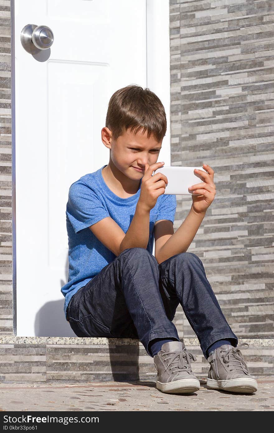 Boy with mobile phone sitting on staircase in front of a door