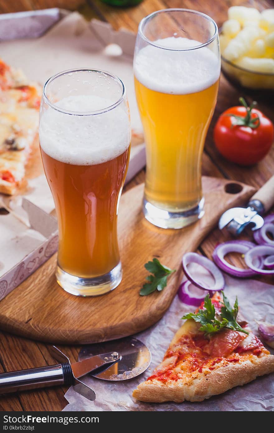 Two glasses of beer with hot pizza on an old wooden table.