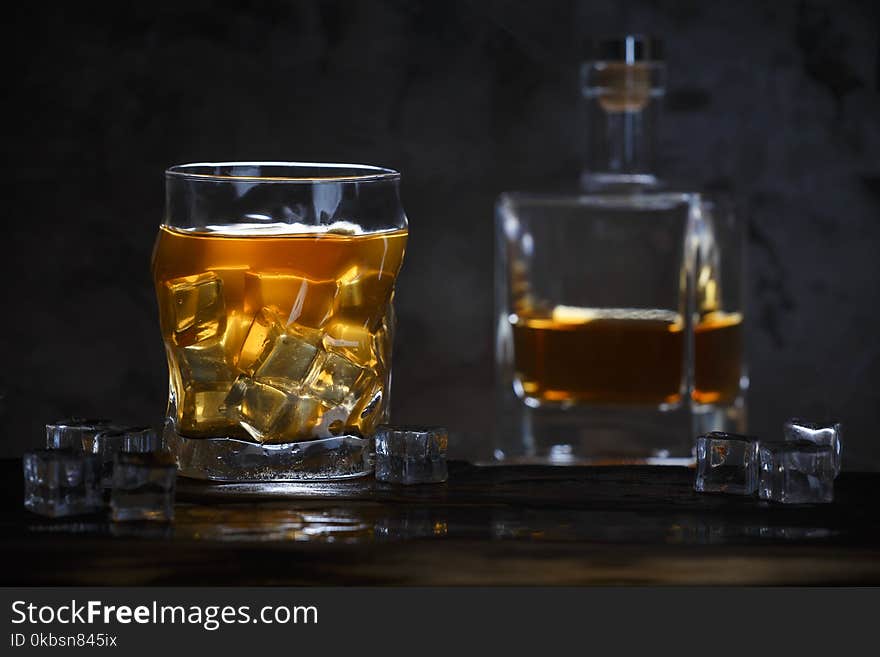 Alcohol in glass with ice and in bottle on dark background