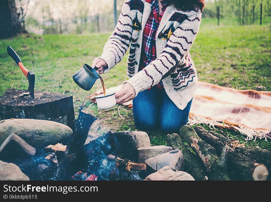 A girl is drinking coffee by the fire.