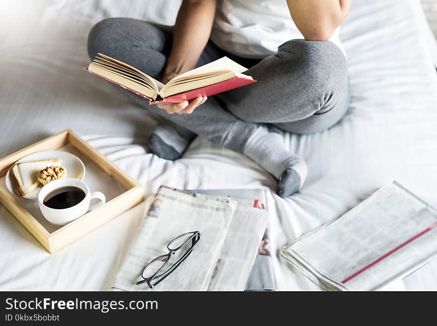 Woman reading book or newspaper and drinking coffee breakfast on bed during the morning