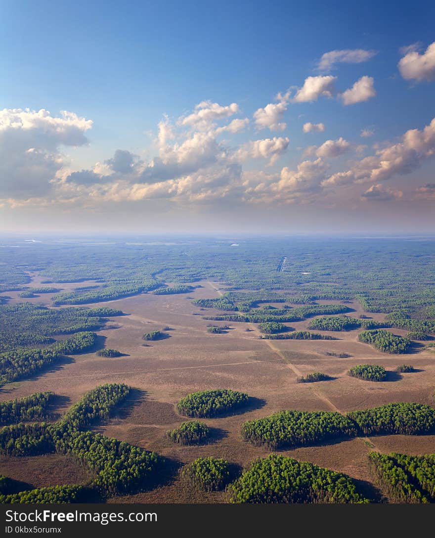 The plain covered with forest and white clouds on the background, bird`s eye view. The plain covered with forest and white clouds on the background, bird`s eye view