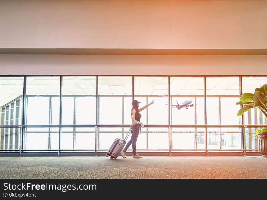 Traveler women plan and backpack see the airplane at the airport glass window, girl tourist hold bag and waiting near luggage in hall airplane departure. Travel Concept.