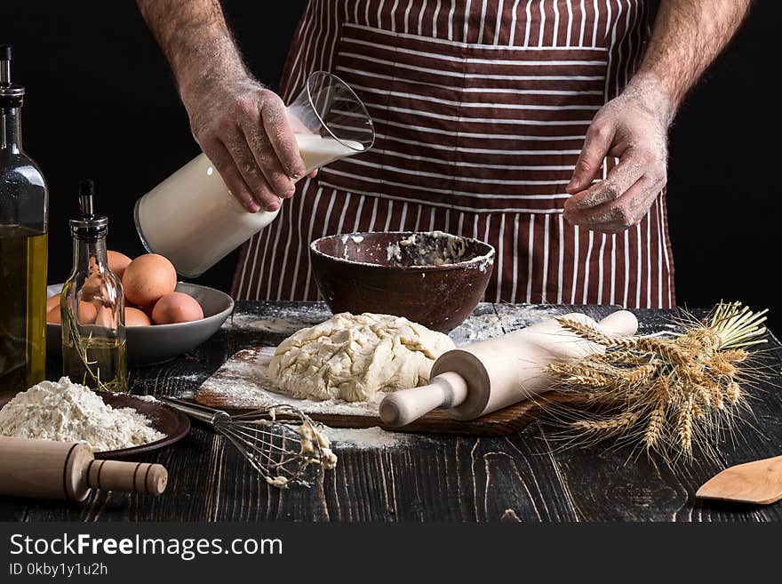 Baker in uniform pouring milk from plastic bottle into bowl. A handful of flour with egg on a rustic kitchen. Ingredients for cooking flour products or dough bread, muffins, pie, pizza dough . Copy space