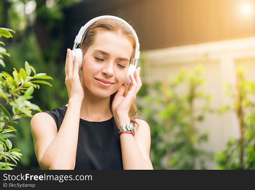 Woman Wearing Black Sleeveless Dress Holding White Headphone at Daytime