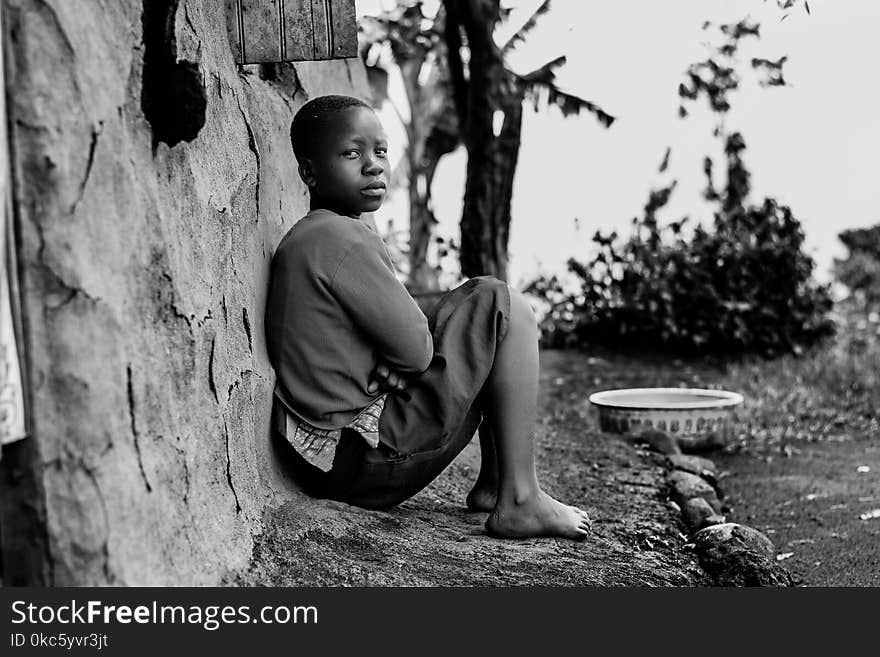 Greyscale Photography of Boy Sitting Behind Wall