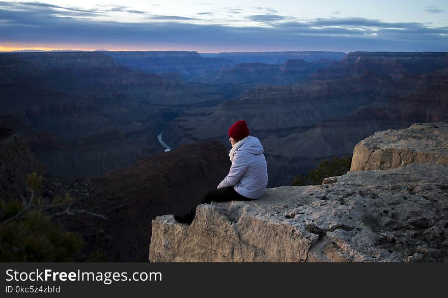 Person Wearing White Hoodie Sitting on Cliff at Daytime