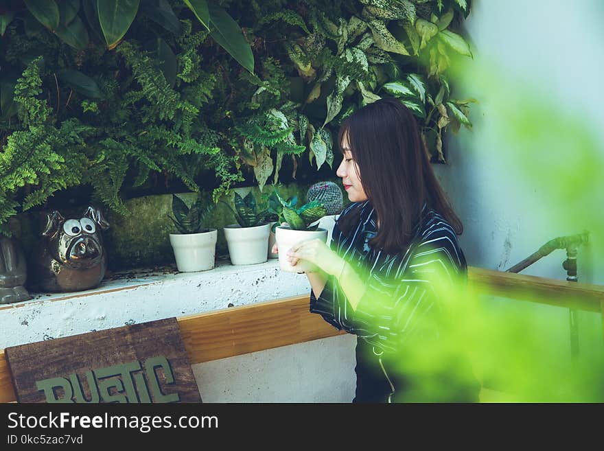 Woman Holding White Clay Pot With Green Plant Sitting Near White Painted Wall