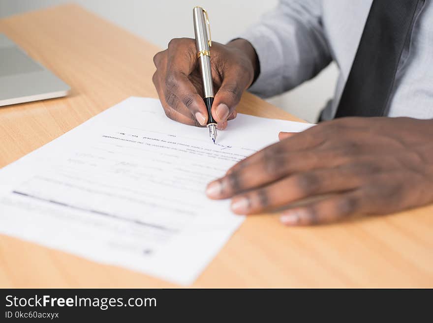 Person Holding Gray Twist Pen and White Printer Paper on Brown Wooden Table