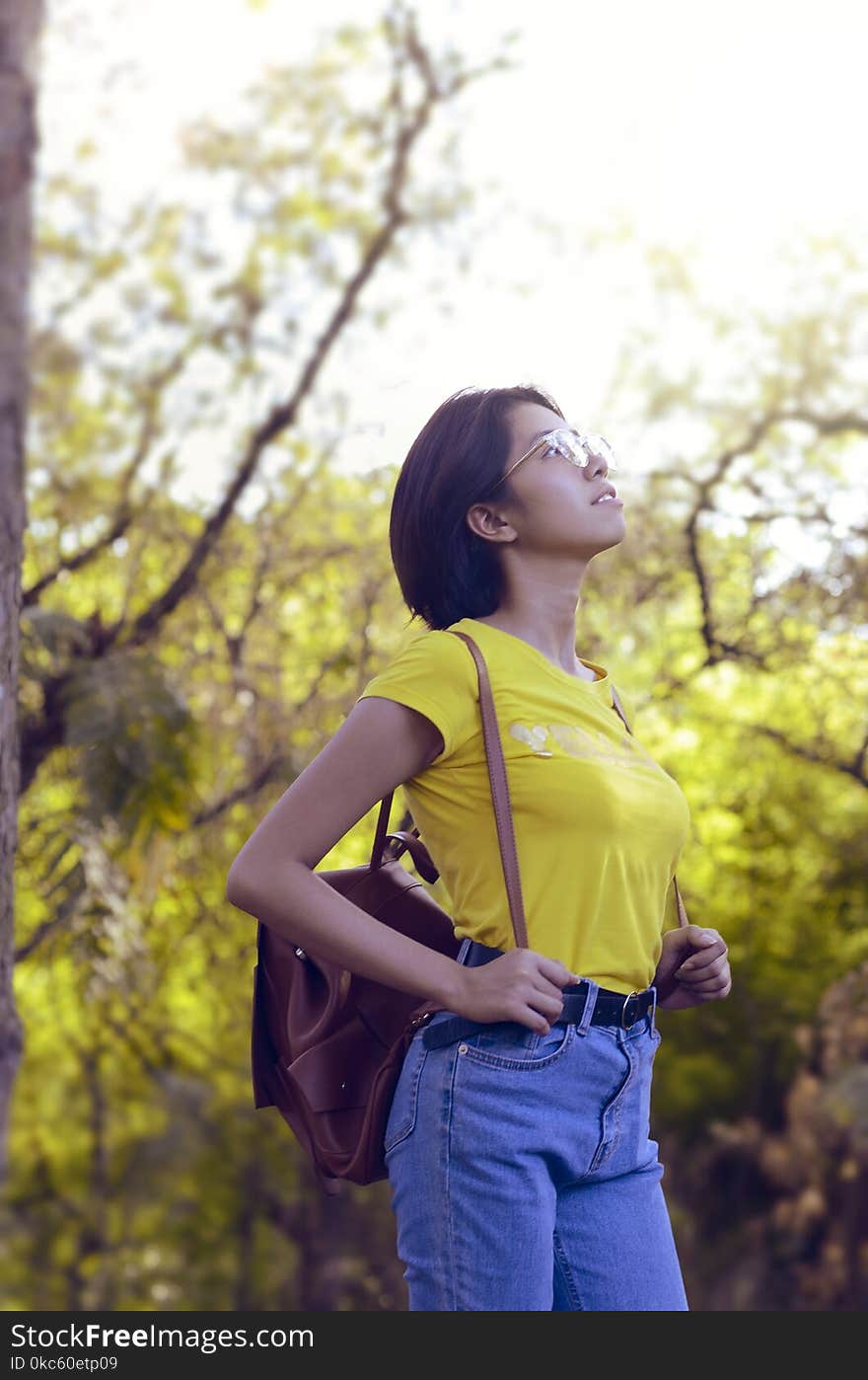 Woman Wearing Yellow Shirt and Looking Up Surrounded by Trees