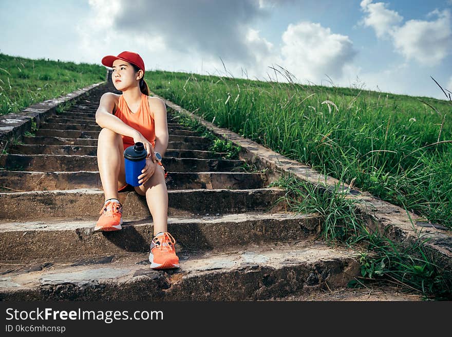 An asian woman athletic is jogging on the concrete road, she is warming her body and tide her tying her shoes tightly fitting before workout.