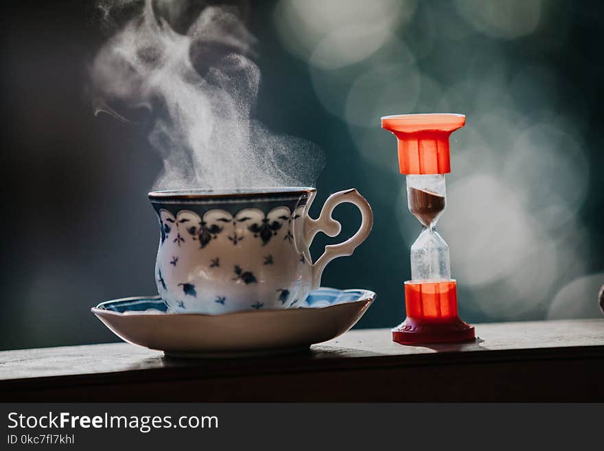 Time to drink tea. A neat cup for tea with a blue pattern and a saucer stand on wooden rails. Near the hourglass. Time to drink tea. A neat cup for tea with a blue pattern and a saucer stand on wooden rails. Near the hourglass