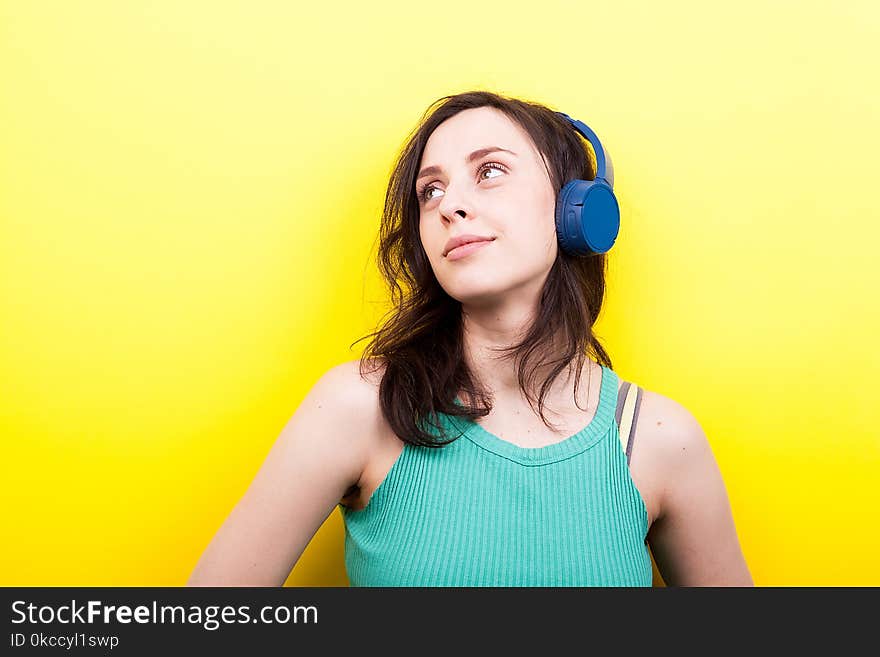 Young woman with eyes up listening to music on yellow background in studio