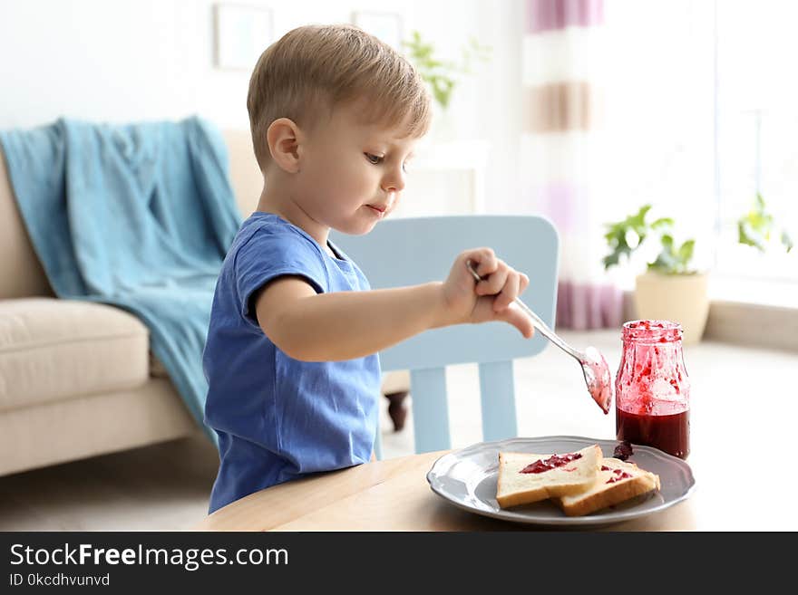 Little boy spreading jam on toasts at table