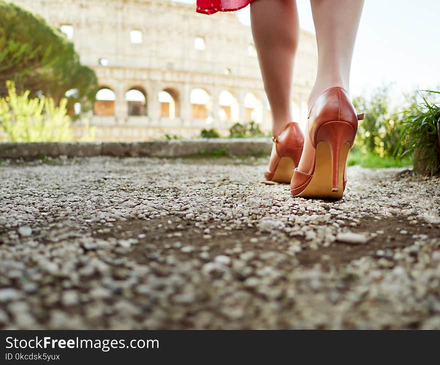 Crop shot of female feet in elegant high heels walking on alley with Colosseum on background.