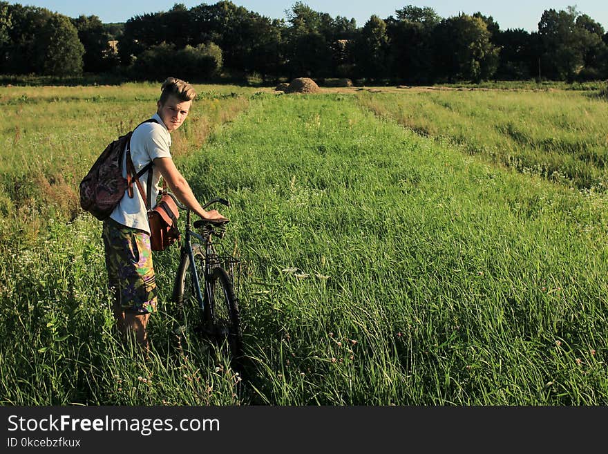 Boy holding and riding a bicycle in a field on a sunny summer da