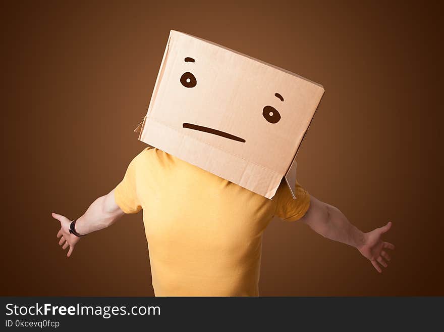 Young man gesturing with a cardboard box on his head with straight face