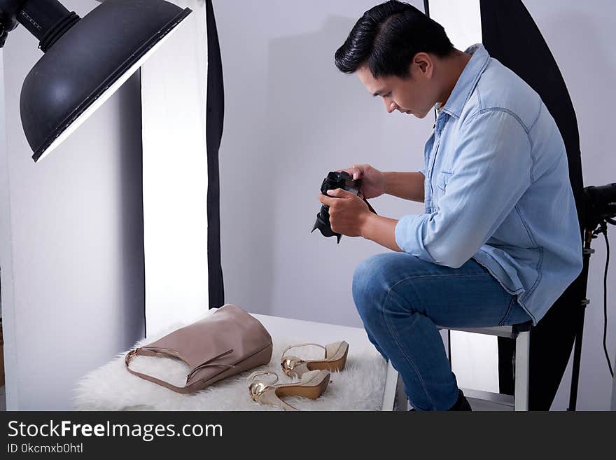 Young Vietnamese man taking photos of fashion items in studio. Young Vietnamese man taking photos of fashion items in studio