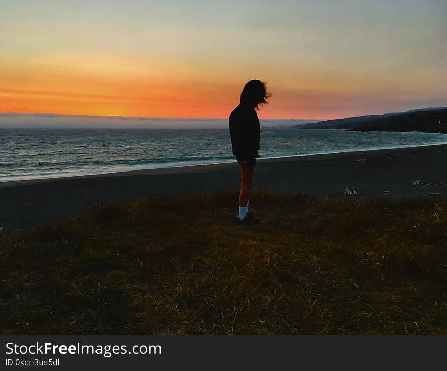 Person Standing on Seashore during Sunset