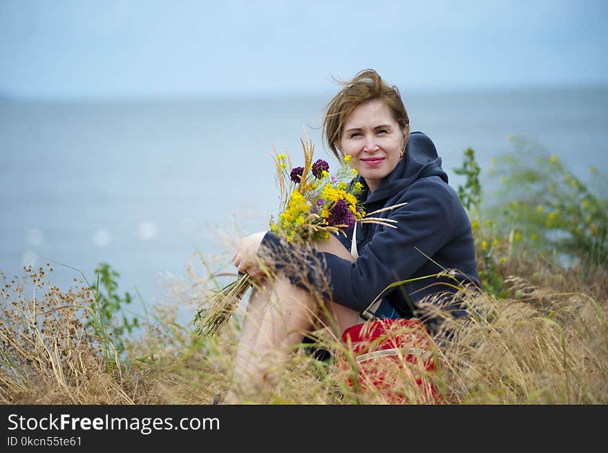 Woman Sitting on Grass Holding Flowers Wearing Black Hoodie