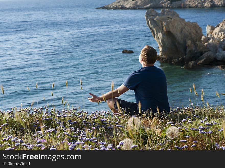 Man Sitting on Flower Fields Facing Ocean